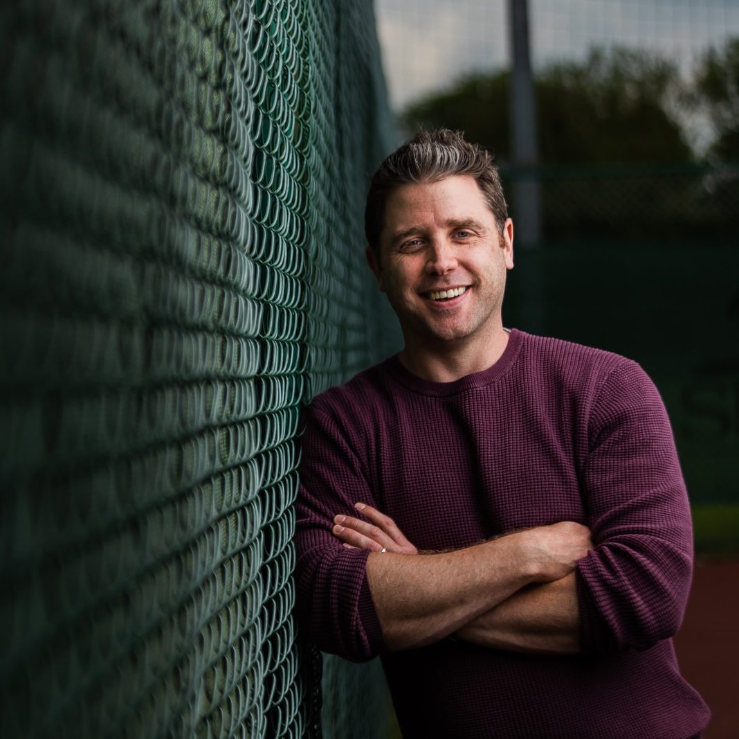 man in maroon crew neck t-shirt leaning on green metal fence during daytime